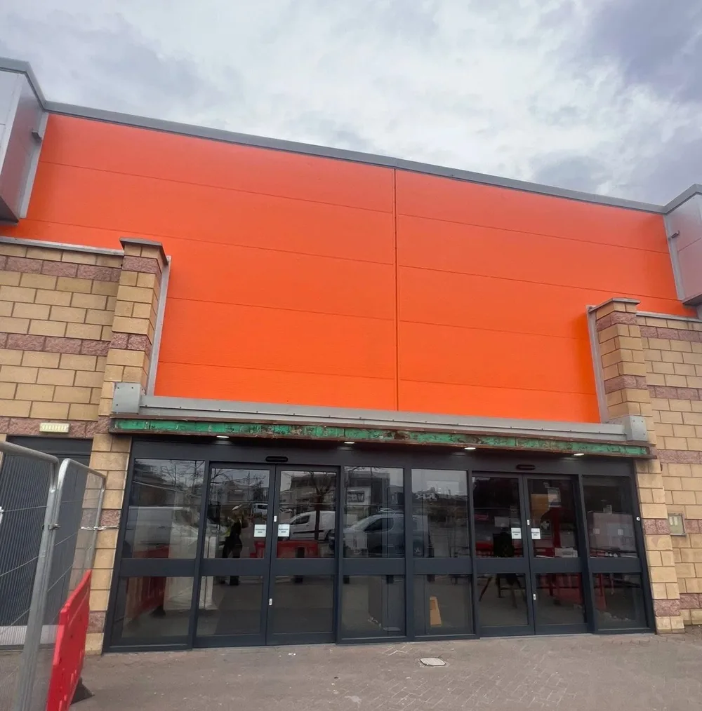 Retail store entrance with sprayed dark grey doors and surround beneath an orange fascia