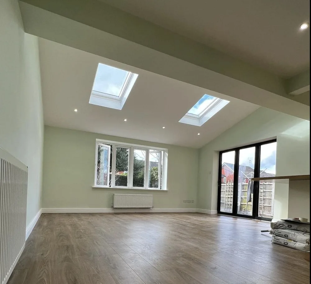 Open-plan kitchen extension painted in soft sage with a white vaulted ceiling